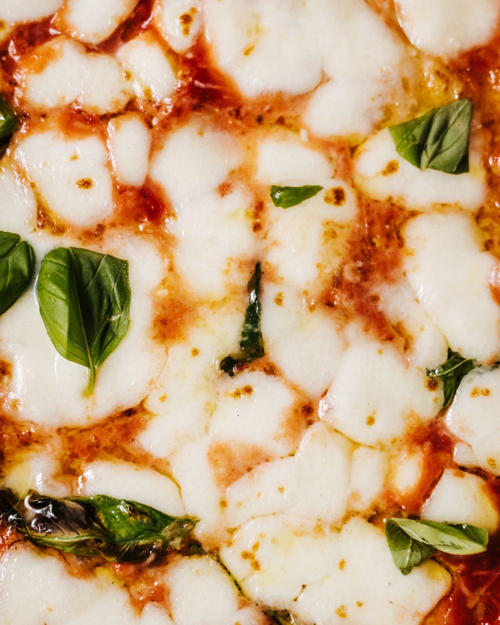 Close view of melted mozzarella, tomato, and basil on a baked pizza