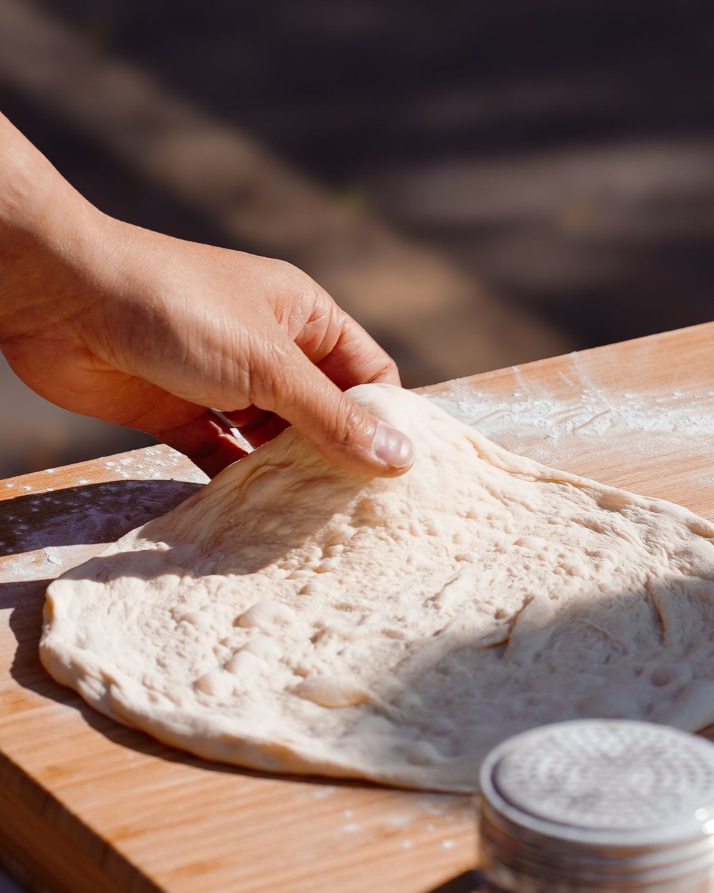 Hands stretching a round of pizza dough on a floured wooden board
