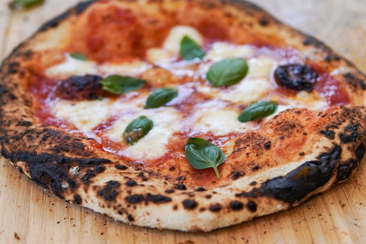 A wood-fired margherita pizza with blistered crust, torn mozzarella, and fresh basil on a wooden board
