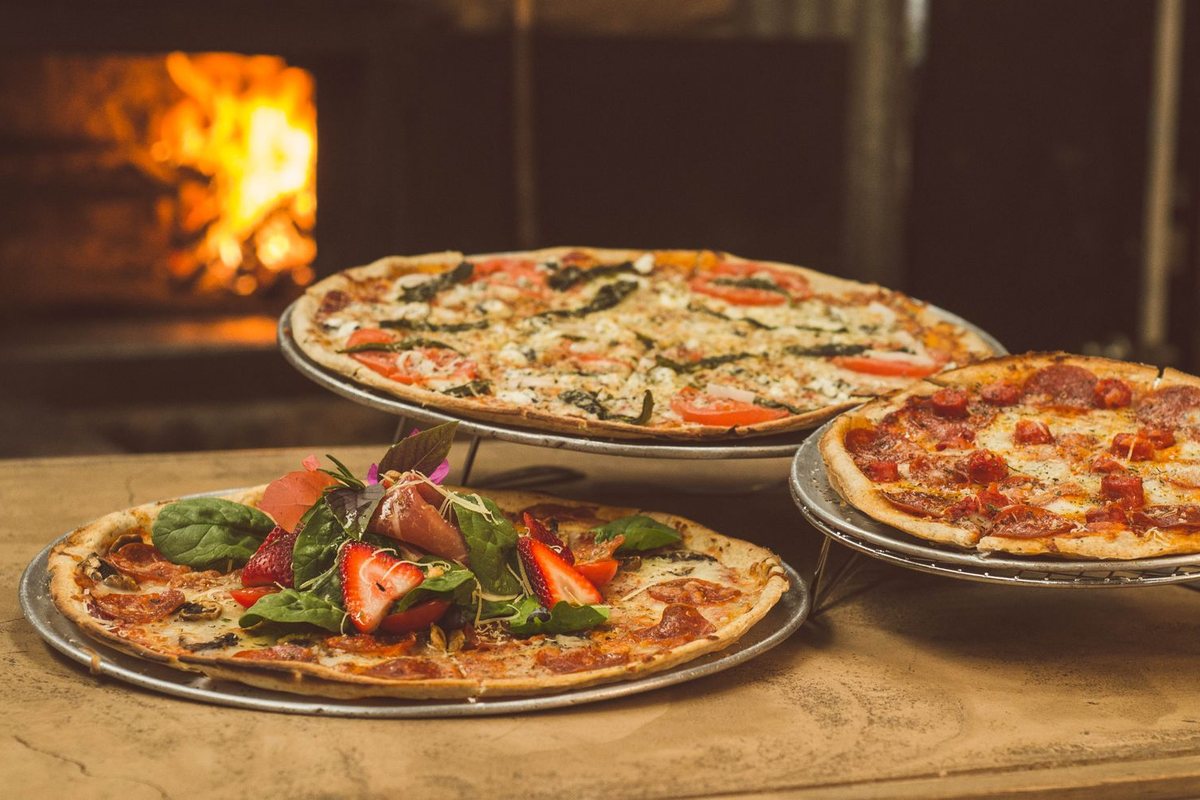 Three finished pizzas on metal stands in front of a lit oven